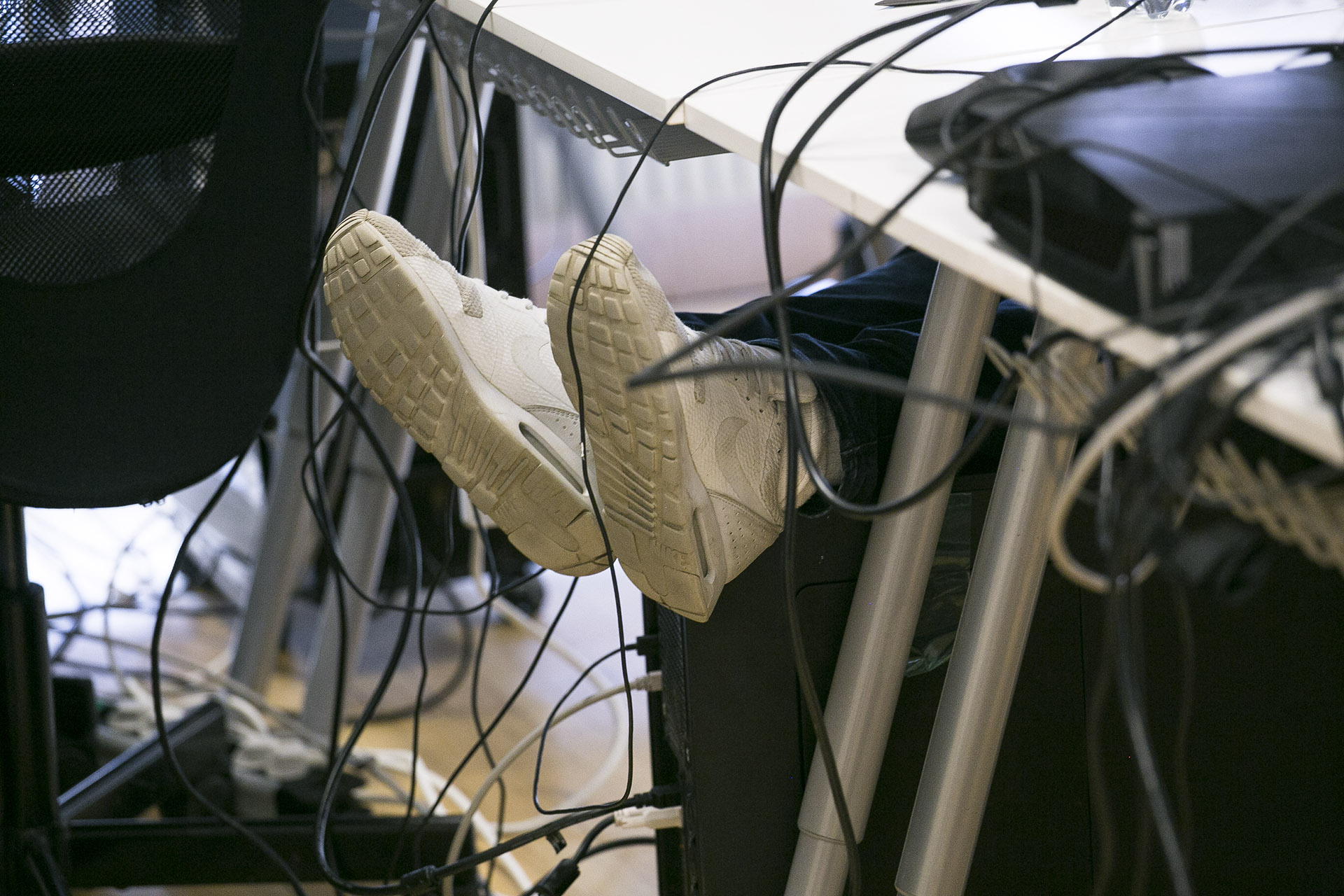 Shoes under a desk with lots of cables from a computer in a game programming classroom