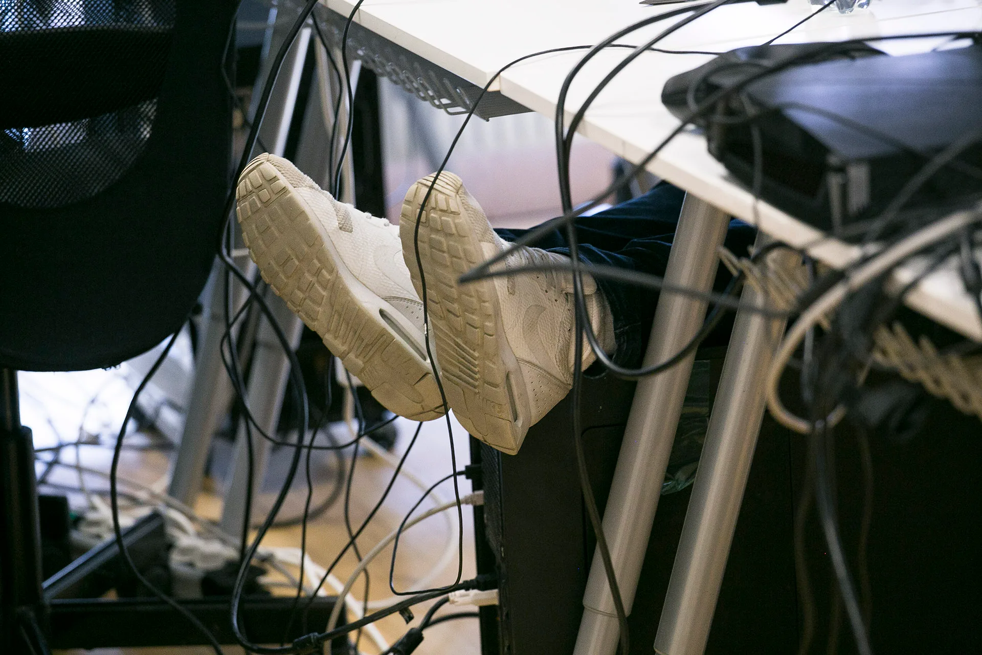 Shoes under a desk with lots of cables from a computer in a game programming classroom